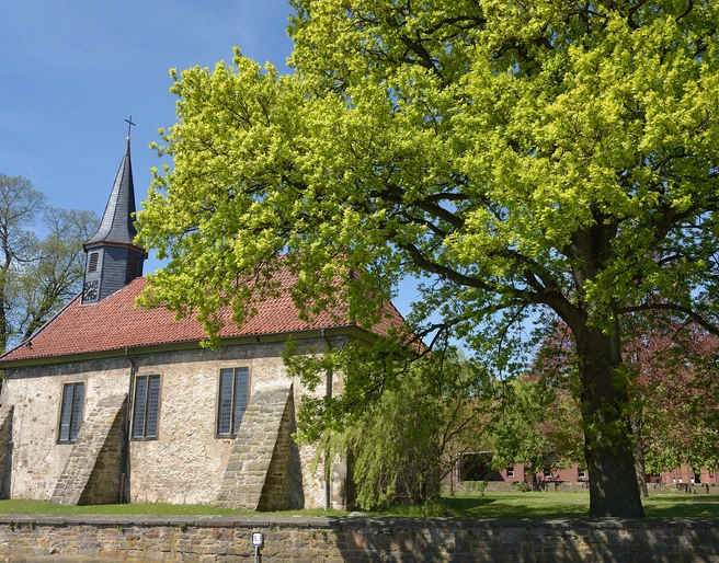 Kirche Münchehagen Historische Kirche in Münchehagen mit rotem Ziegeldach, umgeben von blühenden Bäumen im Frühling.