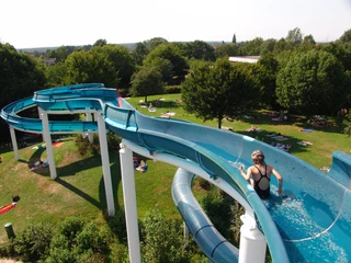 Freibad Münchehagen Person gleitet fröhlich eine große Wasserrutsche im Freibad hinunter, umgeben von grünen Bäumen.