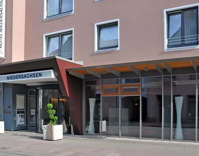 hotel-niedersachsen-haupteingang Hoteleingang mit Glasfront und Vordach, modernes Design mit schlichten Linien und klarer Struktur.