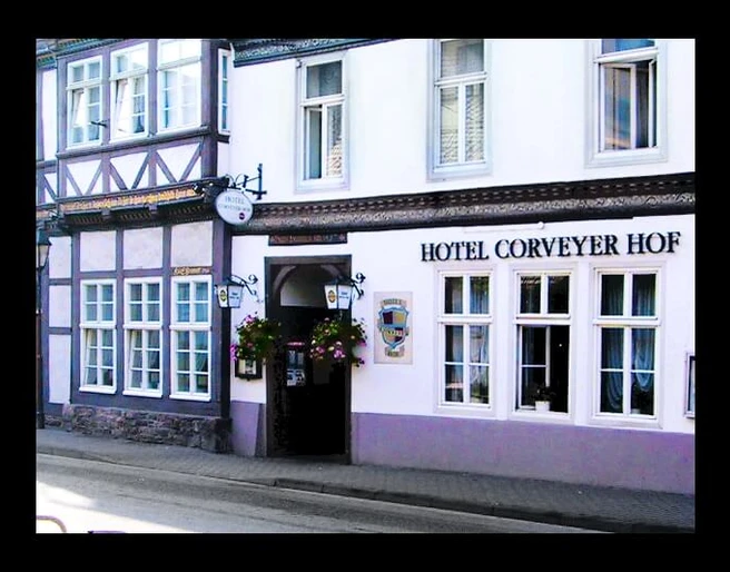 hotel-corveyerhof-hausansicht Fachwerkhaus mit Schild "Hotel Corveyer Hof" an der Fassade, Fenster mit Blumenkästen dekoriert.