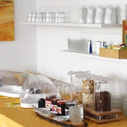 pension-zurweser-fruehstueck Frühstücksbuffet mit Cerealien, Marmelade und Saft, vor warmen Erdfarben und schlichtem Geschirr.