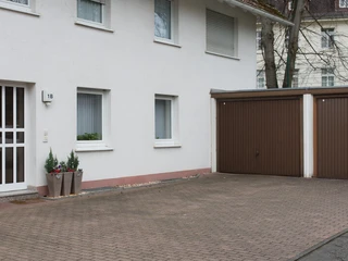 fewo-startpunkt1-garage Zweistöckiges Gebäude mit hellem Putz, daneben braune Doppelgarage, bepflanzte Blumenbehälter vorn.