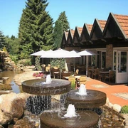 Außenansicht Restauranteingang mit Terrasse, Sonnenschirmen, Springbrunnen und einem kleinen Teich im Grünen.