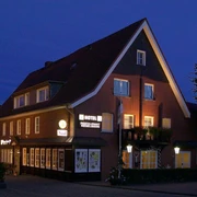 Außenansicht Backsteingebäude mit spitzem Giebeldach, beleuchteten Fenstern und Hotel-Restaurant-Schriftzug bei Nacht.
