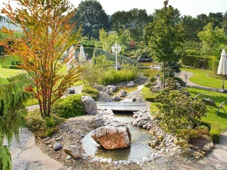 Garten des Ringhotel Teutoburger Wald in Tecklenburg Brochterbeck Gartenlandschaft mit plätscherndem Bach, weißen Schirmen und vielfältiger Bepflanzung im Ringhotel.