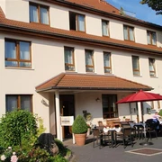 Frühstückstische draußen Hotel Hollmann Sonnige Terrasse mit gedeckten Tischen vor Hotel Hollmann, rote Schirme spenden Schatten.