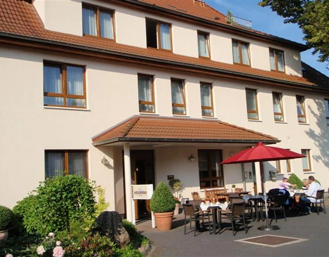 Frühstückstische draußen Hotel Hollmann Sonnige Terrasse mit gedeckten Tischen vor Hotel Hollmann, rote Schirme spenden Schatten.