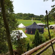 Zeltplatz Abenteuerland Warbug Zelte stehen auf einer grünen Wiese, umgeben von Bäumen und einem rustikalen Holzzaun.