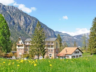 Aussenansicht des Hotels Kurhaus Grimmialp im Sommer Hotelgebäude aus der Belle Epoque inmitten einer blühenden LöwenzahnwieseHotel building from the Belle Epoque in the middle of a flowering dandelion meadowBâtiment d'hôtel Belle Époque au milieu d'une prairie de pissenlits en fleurs