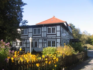 img_0716 Historisches Fachwerkhaus mit roten Dachziegeln, umgeben von blühendem Garten und Holzzaun im Sommer.
