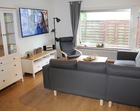 Bei Pohls Ein moderner Wohnbereich mit grauem Sofa, Sessel, Flachbildschirm und großen Fenstern.