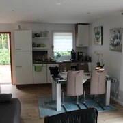 Ein einladendes Wohnzimmer mit Esstisch, offener Küche und großen Fenstern für viel Tageslicht.