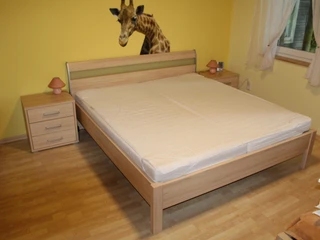 Ein schlichtes Doppelbett aus Holz mit zwei Nachttischen, vor einer gelben Wand mit Giraffenmotiv.