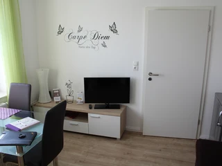 Gästezimmer Bär Helles Gästezimmer mit moderner Einrichtung, Wandtattoo "Carpe Diem" über TV, helle Vorhänge.
