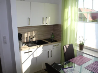 Gästezimmer Bär Helles Gästezimmer mit moderner Küchenzeile, Essbereich, Tageslicht und Blick auf rote Dachziegel.