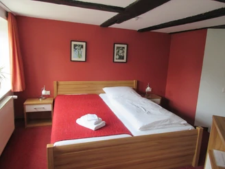 Doppelzimmer im Hotel mit Holzbett, roten Wänden und Bettläufer, Dachbalken an der Decke.