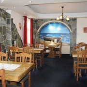 Rustikales Interieur mit Holztischen, roten Vorhängen und Wandgemälde eines Bootes am Strand.