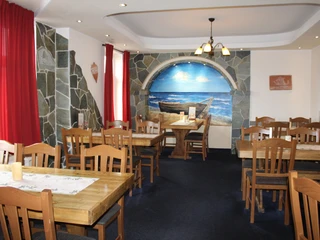 Rustikales Interieur mit Holztischen, roten Vorhängen und Wandgemälde eines Bootes am Strand.