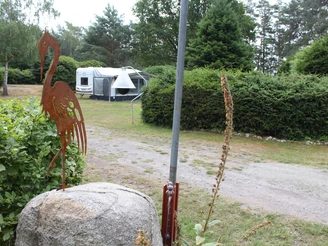 Campingplatz mit einem Wohnwagen im Grünen, rustikale Flamingo-Skulptur und üppige Vegetation.