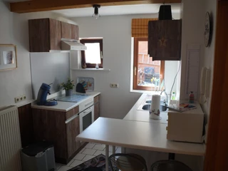 Ferienwohnung Wehrmann Kompakte Küche mit Herd, Kaffeemaschine, Spüle und Holzmöbeln, mit Blick auf ein helles Fenster.