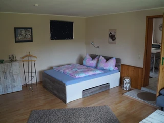 Ferienwohnung Wehrmann Ferienwohnung mit Doppelbett, bunter Bettwäsche und Holzfußboden; Zugang zu einem gefliesten Badezimmer.