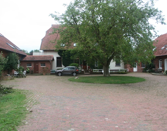 Riederhof 26 Hofgebäude umschließen einen gepflasterten Innenhof mit Baum und geparktem Auto in ländlicher Umgebung.