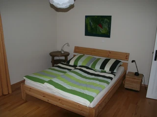 Riederhof 26 Schlafzimmer mit Doppelbett, gestreifter Bettwäsche, Nachttisch, Lampe und Kunstwerk an der Wand.