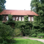 Historisches Herrenhaus mit roter Ziegelbedachung und von Efeu überwucherten Fassaden. Umgeben von üppigem Grün.