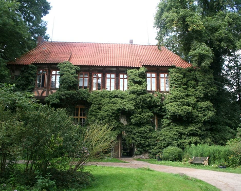 Rittergut Brokeloh Historisches Herrenhaus mit roter Ziegelbedachung und von Efeu überwucherten Fassaden. Umgeben von üppigem Grün.