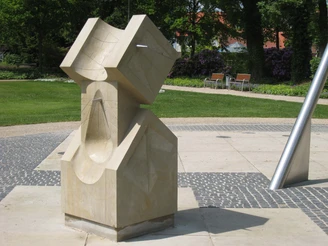 "Sonnenuhr" von Klaus Wolf Simon Sonnenuhr-Skulptur aus hellem Stein im Park, umgeben von Grünflächen und Bäumen, zeitlos designt.