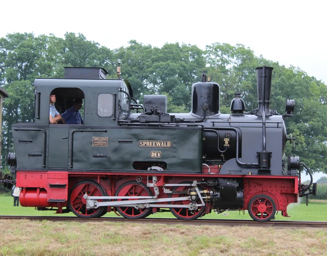 Museums-Eisenbahn Bruchhausen-Vilsen Historische Dampflok namens "Spreewald" auf einer grünen Wiese mit Bäumen im Hintergrund, seitlich fotografiert.