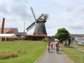 Historische Windmühle in Niedersachsen umgeben von grünen Wiesen, im Vordergrund radelnde Besucher.