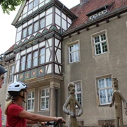 Altes Amtsgericht Zwei Radfahrerinnen mit Helmen betrachten moderne Bronzefiguren vor einem Fachwerkgebäude.