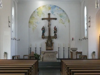 Der Innenraum der St. Joseph Kirche zeigt eine Altaransicht mit Holzkreuz, Heiligenfiguren und Wandgemälde im Hintergrund.