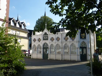 Liborius-Trinkhalle in Bad Lippspringe Historische Liborius-Trinkhalle in Bad Lippspringe vor einer Kirche, umgeben von Laubbäumen.