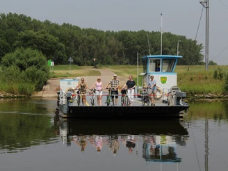 Weserfähre Schweringen Menschen auf einer kleinen, über einen Fluss fahrenden Fähre mit Fahrrädern, umgeben von Natur.