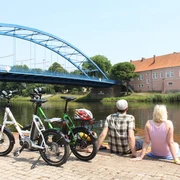 Grafenschloss zu Hoya Ein Paar sitzt entspannt am Wasser, mit Blick auf das historische Grafenschloss zu Hoya und eine blaue Brücke.