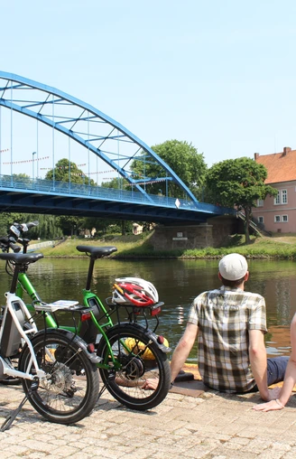 Grafenschloss zu Hoya Ein Paar sitzt entspannt am Wasser, mit Blick auf das historische Grafenschloss zu Hoya und eine blaue Brücke.