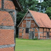 Schafstallviertel Hülsen Zwei historische Fachwerkgebäude mit Backsteinwänden stehen auf einer grünen Wiese vor Bäumen.