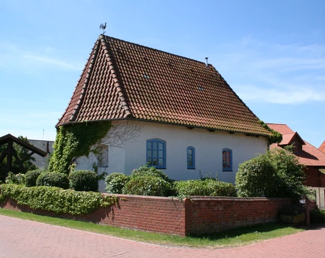 Alte Kapelle in Haßbergen mit rotem Ziegeldach, weißen Mauern und umgeben von grüner Hecke.