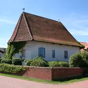 Alte Kapelle Haßbergen Alte Kapelle in Haßbergen mit rotem Ziegeldach, weißen Mauern und umgeben von grüner Hecke.
