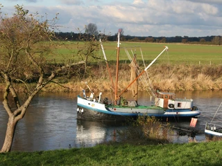 Drakenburg Aalschokker Aalschokker auf der Weser vor Drakenburg, umgeben von Wiesenlandschaft und bewölktem Himmel.