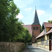 Straße führt zu einer historischen Backsteinkirche mit spitzem Turm, flankiert von Fachwerkhäusern.