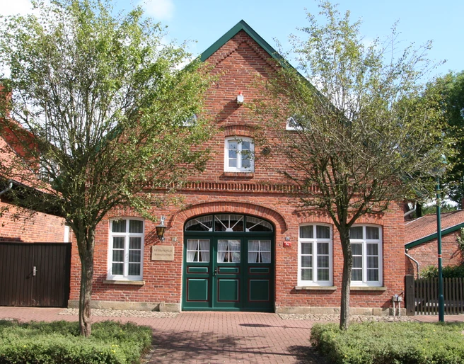 Witten Hus Liebenau Backsteinhaus mit grünen Doppeltüren, weißen Fenstern und einladender Fassade, flankiert von Bäumen.