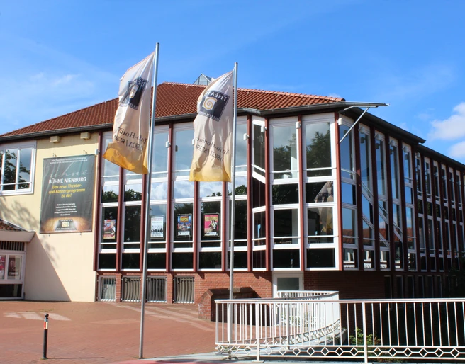 Kulturzentrum mit markanten Glasfassaden und Wimpel vorm Haupteingang, blauer Himmel im Hintergrund.