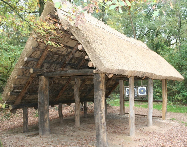Nachbau Altsachsenhütte Rekonstruktion eines historischen altsächsischen Langhauses mit strohgedecktem Dach in einem Wald.