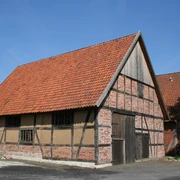 Fachwerkhaus mit rotem Ziegeldach und Holztür in Liebenau, umgeben von Bäumen und klarer Himmel.