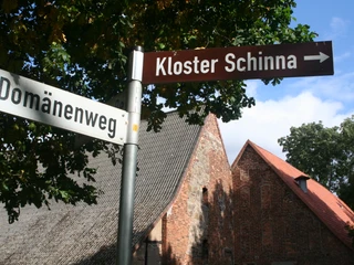 Kloster Schinna Wegweiser in der Nähe von historischem Backsteingebäude des Klosters Schinna unter blauem Himmel.