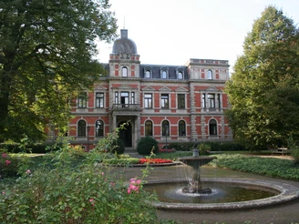 Schlosspark Etelsen Historisches Schloss mit Grünanlage und zentralem Springbrunnen, umgeben von gepflegtem Park.