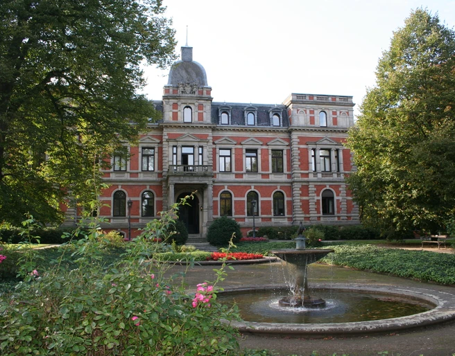 Schlosspark Etelsen Historisches Schloss mit Grünanlage und zentralem Springbrunnen, umgeben von gepflegtem Park.